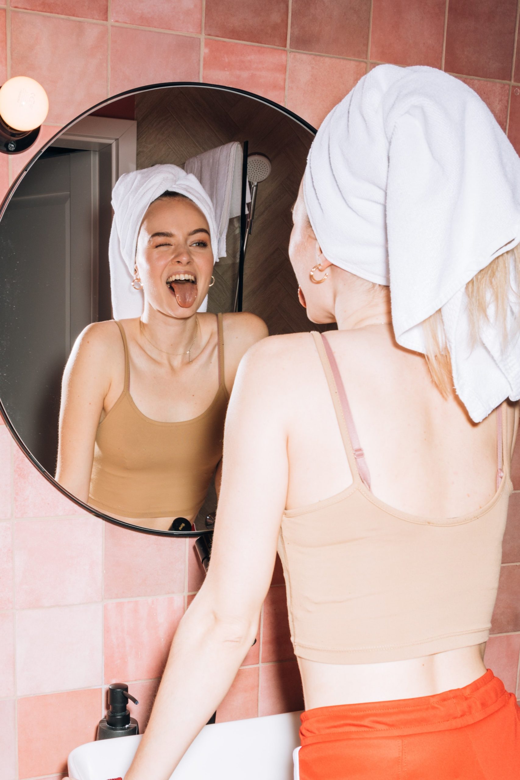 a woman with a towel on her head looks into a mirror winking and sticking her tongue out