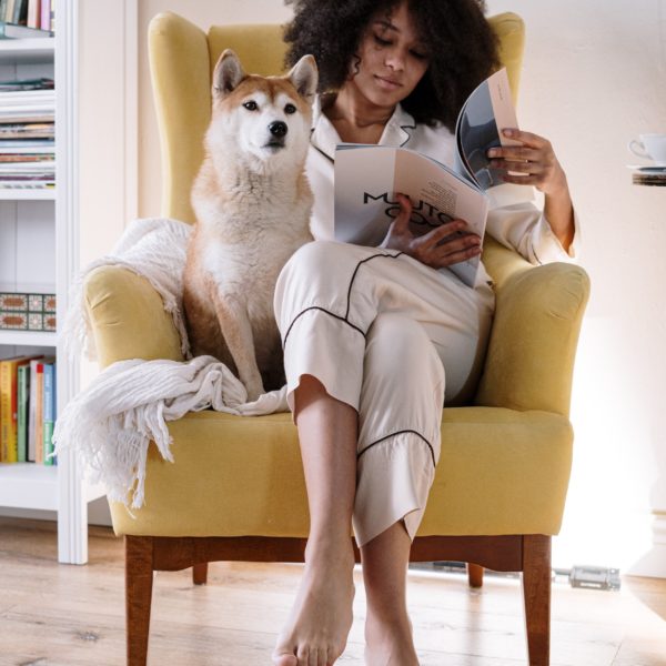 woman sitting in a chair reading a magazine with a dog next to her
