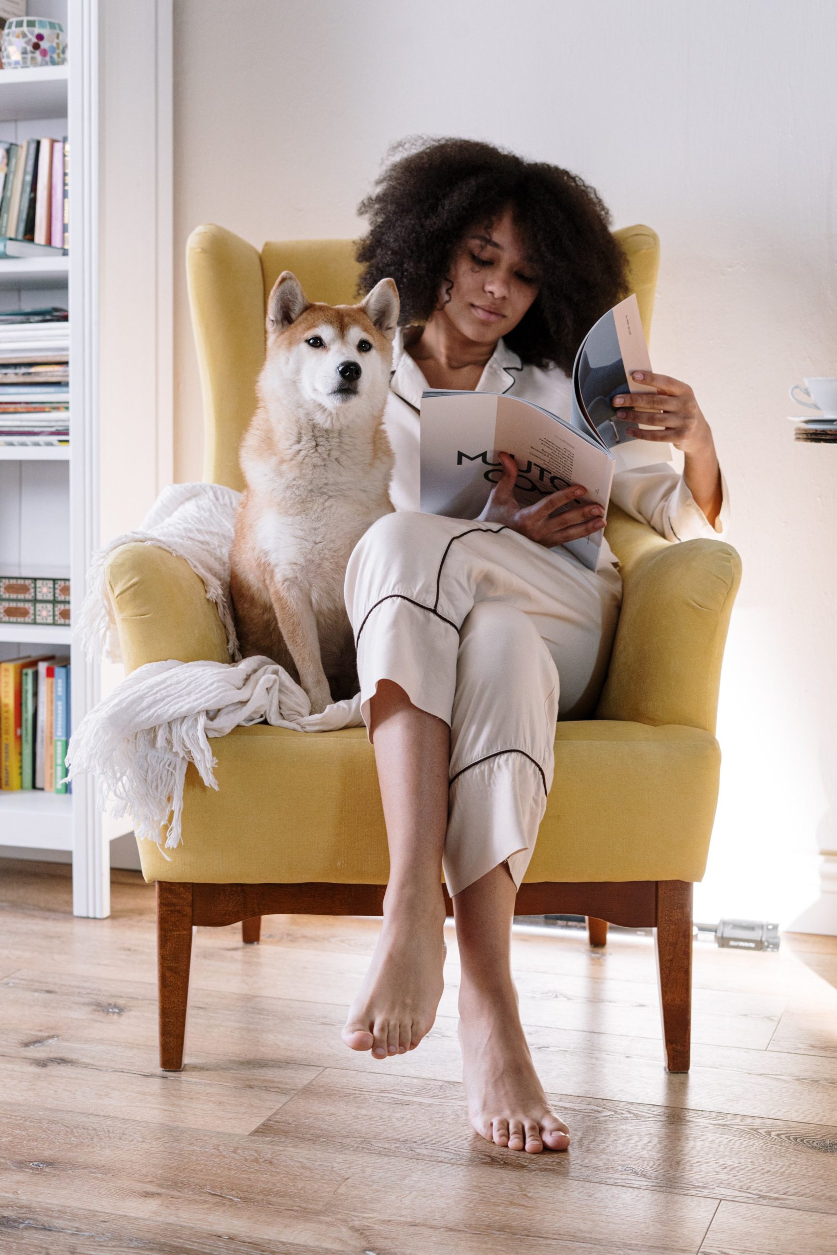 woman sitting in a chair reading a magazine with a dog next to her