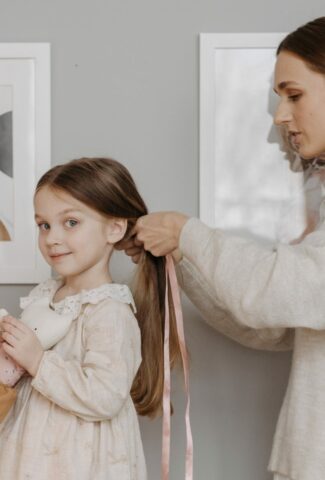 A mother tying her daughter's hair with a ribbon