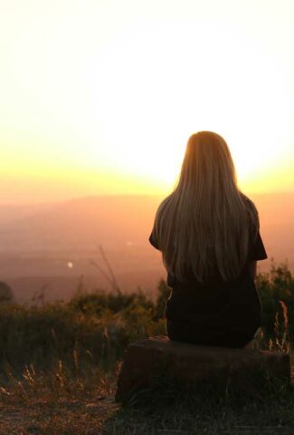 Silhouette of a woman looking at sunset at an overlook with back to the camera.
