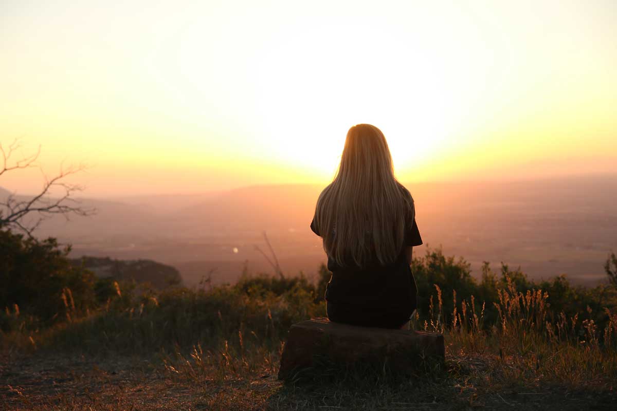 Silhouette of a woman looking at sunset at an overlook with back to the camera.