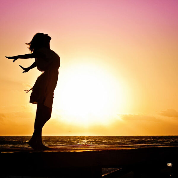 Silhouette profile image of woman with arms back and sunsetting in background