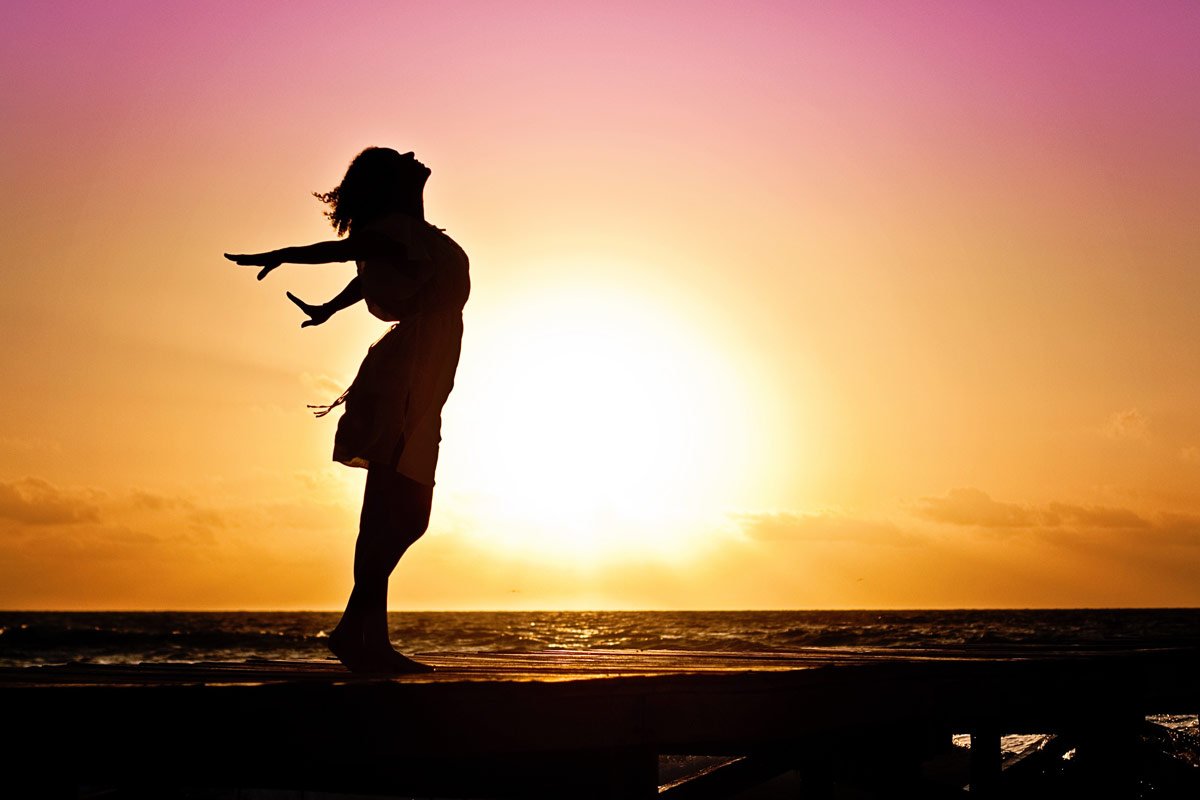 Silhouette profile image of woman with arms back and sunsetting in background